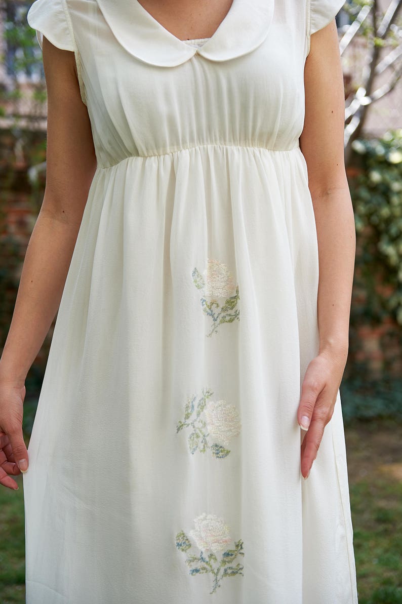 May include: A white sleeveless dress with a Peter Pan collar and embroidered white roses.
