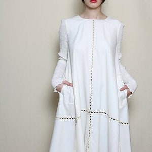 May include: A white long-sleeved dress with a round neckline and a slightly flared skirt. The dress has a decorative stitch detail around the neckline, hem, and pockets.