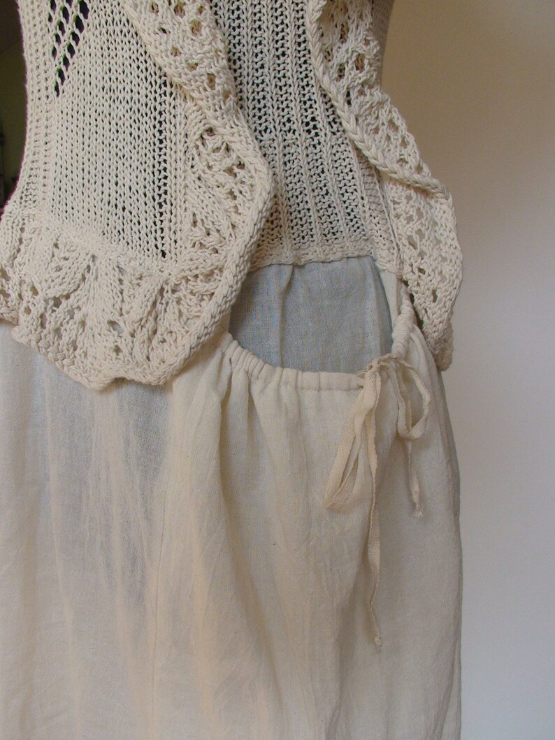 May include: A white crocheted top with a gathered skirt and a drawstring closure. The top has a delicate lace pattern and the skirt is made of a soft, lightweight fabric.