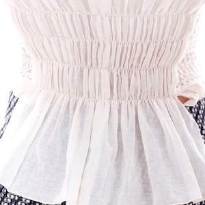 May include: White cotton blouse with a gathered elastic waistband and a ruffled hem.