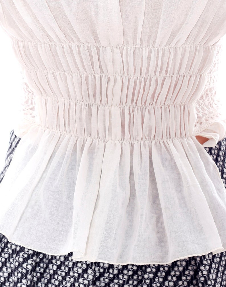 May include: White cotton blouse with a gathered elastic waistband and a ruffled hem.