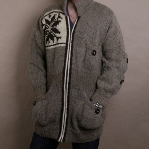 May include: A gray knitted cardigan with a white and brown snowflake design on the front. The cardigan has a zipper closure and two pockets.