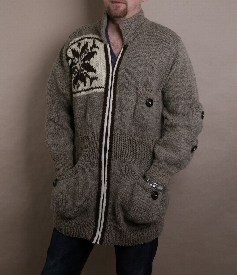 May include: A gray knitted cardigan with a white and brown snowflake design on the front. The cardigan has a zipper closure and two pockets.