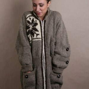 May include: A gray knitted cardigan with a brown and white patterned design on the front. The cardigan has a zipper closure and two large pockets.