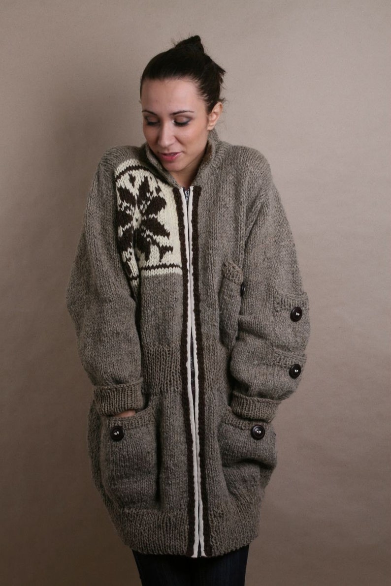 May include: A gray knitted cardigan with a brown and white patterned design on the front. The cardigan has a zipper closure and two large pockets.