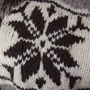 May include: A close-up of a knitted sweater with a brown snowflake pattern on a white background.