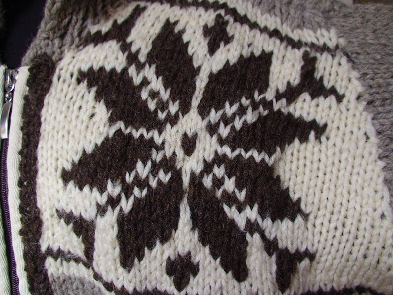 May include: A close-up of a knitted sweater with a brown snowflake pattern on a white background.