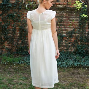 May include: A white maxi dress with a simple design and a slightly gathered waist. The dress has short sleeves and a scoop neckline.