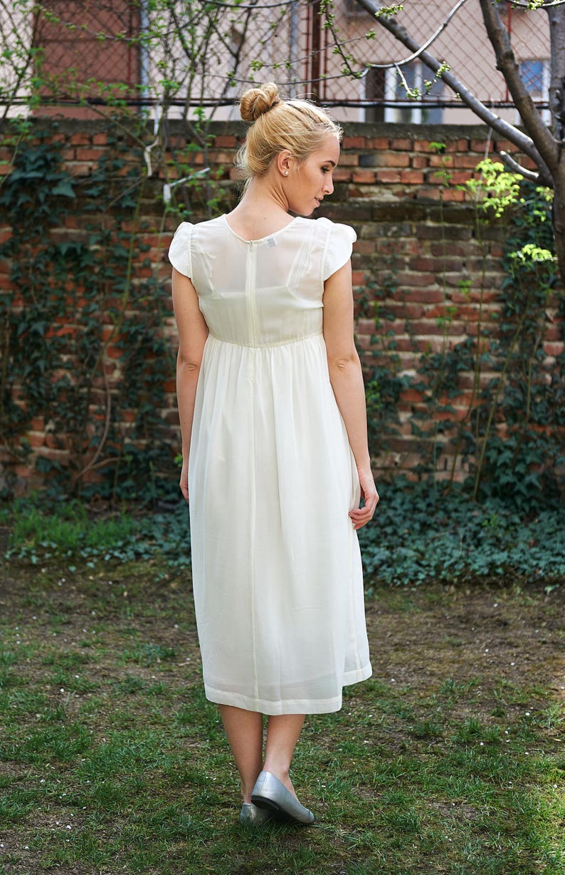 May include: A white maxi dress with a simple design and a slightly gathered waist. The dress has short sleeves and a scoop neckline.