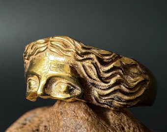 May include: A gold-toned ring with a detailed design of a woman's face with flowing hair.