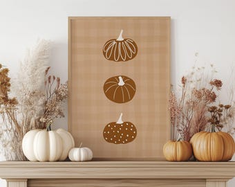 May include: A framed print featuring three brown pumpkin illustrations on a tan plaid background. The print is displayed above a mantel decorated with white and orange pumpkins and dried floral arrangements. The text "WE PRINT & SHIP FOR FREE IN THE U.S." is visible.