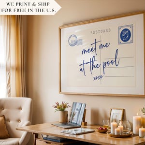 May include: A framed postcard print with the text "meet me at the pool" in navy blue script. The print includes a postage stamp design and is displayed above a wooden desk with a laptop, candles, and other decor.