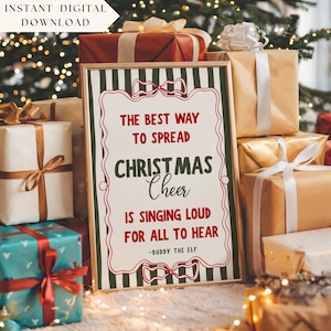 May include: A framed print with the text "THE BEST WAY TO SPREAD CHRISTMAS CHEER IS SINGING LOUD FOR ALL TO HEAR - BUDDY THE ELF." The print is surrounded by wrapped gifts in various colors, including gold, red, and teal.
