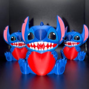 K&ouml;nnte beinhalten: Drei blaue und rote Stitch-Figuren sind in einer Reihe angeordnet. Jede Figur hat gro&szlig;e Ohren, ein breites Grinsen und h&auml;lt ein rotes Herz. Die Figuren sitzen auf einer reflektierenden Oberfl&auml;che.