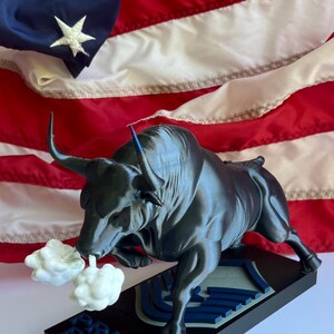 May include: A dark gray bull figurine with white smoke-like accents, mounted on a black base with blue text that reads "PRIME BEEF". The background features an American flag.