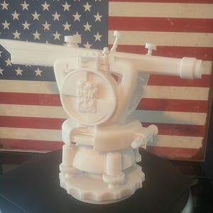 May include: A white 3D printed model of a US Navy surveying instrument. The instrument has a telescope, a tripod, and a circular base with the letters "USN" inscribed on it.