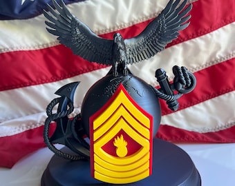 May include: A black and yellow decorative emblem featuring an eagle with outstretched wings atop a globe, an anchor, and a hand holding a globe. A yellow and red chevron is in the center. The base is dark blue with the words "Semper Fidelis" in red.