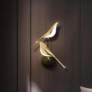 May include: A pair of gold bird-shaped wall sconces with a modern design. The sconces are mounted on a wall and have a minimalist aesthetic.