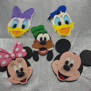 May include: A collection of colorful character face decorations, including Mickey Mouse, Minnie Mouse, Donald Duck, Daisy Duck, and Goofy. Each character is rendered in a cartoon style with bright colors and distinct features.
