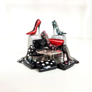 May include: A collection of miniature high-heeled shoes and purses in various colors and patterns. The shoes include red, black with pink polka dots, and black with teal polka dots. The purses are black with white polka dots and red glitter.