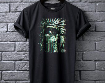 May include: A black short-sleeve t-shirt featuring a central graphic print of a person wearing a feathered headdress with a digital glitch effect in shades of green and white. The text WRAITH IN THE MACHINE is printed in the upper right corner.