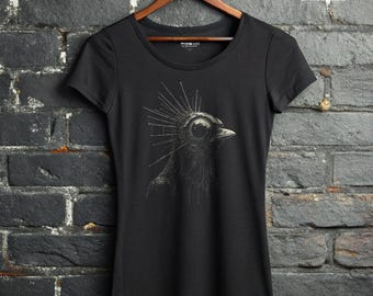 May include: A black short-sleeved t-shirt featuring a detailed graphic of a bird with a mechanical, spiky headpiece. The design is rendered in shades of grey and white. The text WRATH IN THE MACHINE is printed in white at the top right corner.