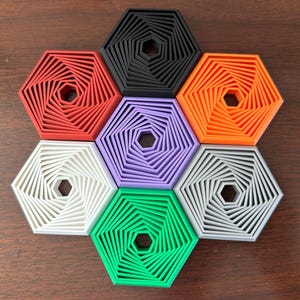 May include: Six hexagonal coasters in different colors, each with a concentric design of smaller hexagons. The colors are red, black, orange, purple, white, and green.