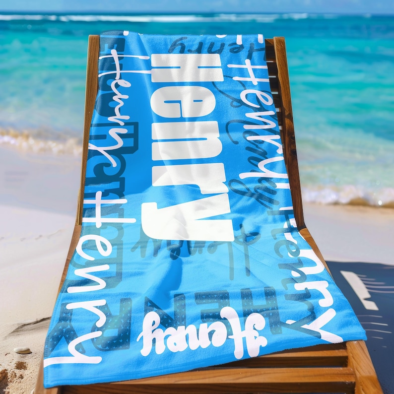Person stands on a sandy beach holding a bright green personalized beach towel with the name Henry in bold and script fonts. Custom name towel, perfect for pool, swim, or summer trips, and a thoughtful gift for any age.