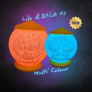 Könnte beinhalten: Zwei leuchtende, kugelförmige Nachtlichter mit den Charakteren Stitch und Lilo. Eines ist orange, das andere blau. Beide haben gelbe Sockel und Deckel. Der Text "Lilo & Stich 02" und "Multi Colour" sind sichtbar. Geeignet für Kinderzimmer.