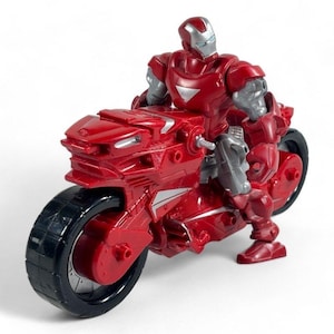 May include: A red and silver action figure of a character riding a red motorcycle. The figure has a silver helmet and gray arms. The motorcycle has black tires and silver accents. The toy is set against a white background.