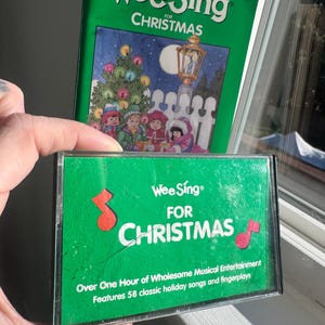May include: A green cassette tape and songbook titled "Wee Sing For Christmas." The cassette features red musical notes and text. The songbook cover shows children around a Christmas tree. The cassette promises over an hour of wholesome musical entertainment.