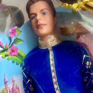 Może przedstawiać: Lalka z brązowymi włosami i niebieskimi oczami, ubrana w królewski niebieski aksamitny strój ze złotymi wykończeniami. Strój lalki ma złote akcenty i wysoki kołnierz. Tło zawiera tropikalną scenerię z różowymi kwiatami i zamkiem.
