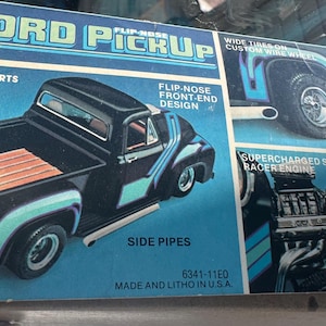 Puede incluir: Caja de modelo de un camión Ford Pickup de 1953. La caja presenta un camión negro con detalles turquesa, una caja de madera y el texto "53 FORD PICKUP". Texto adicional incluye "Bright Plated Parts" y "Molded in Black".