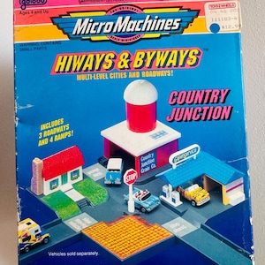 May include: A vintage Micro Machines Hiways & Byways Country Junction playset box. The box is blue, pink, and yellow, with miniature buildings, roadways, and toy vehicles. The box includes the text "Multi-Level Cities and Roadways!"