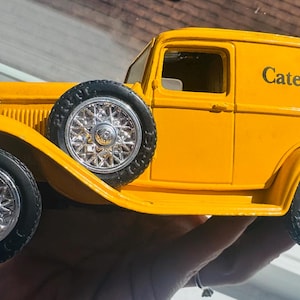 Puede incluir: Un camión de juguete amarillo vintage con el logotipo de Caterpillar en el lateral. El camión tiene neumáticos negros y llantas plateadas. Una rueda de repuesto está montada en el lateral. Un coleccionable clásico.