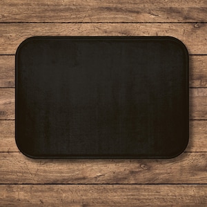 May include: A rectangular black object with rounded corners, set against a backdrop of wooden planks. The object has a textured surface and a solid, dark color, creating a contrast with the wood grain.