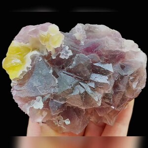 May include: A close-up of a fluorite mineral specimen. The crystal formation displays a mix of colours, including purple, yellow, and clear. The specimen has a crystalline structure with visible facets and a natural, rough texture.