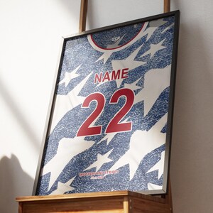 May include: Framed print of a jersey design with a blue and white star pattern. The jersey features the word "NAME" above the number "22" in red. The text "USA" is at the top.