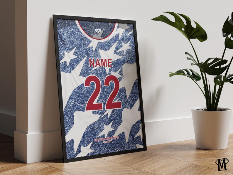 May include: Framed print of a USA soccer jersey design. The jersey features a blue and white star pattern with the number 22 in red. The word "NAME" is above the number. The top of the jersey has the word "USA".