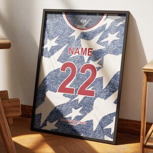 May include: Framed print of a jersey design with a distressed look. The jersey features a blue and white star pattern, with the word "NAME" above the number "22" in red. The word "USA" is at the top.