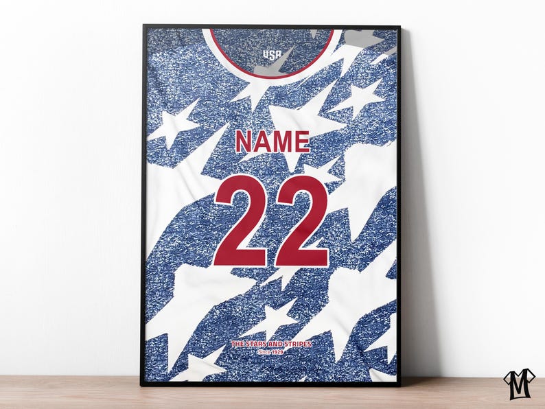 May include: Framed print of a USA soccer jersey. The jersey design features a blue background with white stars and stripes. The number "22" is displayed in red, with the word "NAME" above it. The text "THE STARS AND STRIPES" is at the bottom.