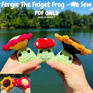 May include: Crocheted fidget frogs with flower, mushroom, and sunflower designs. The frogs are light green with black eyes and are topped with red, yellow, and pink crocheted elements. Text on the image reads "Fergie The Fidget Frog - No Sew PDF ONLY @KatCrochetsComforts."