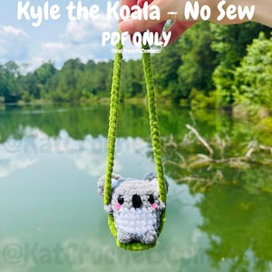 May include: A handmade crochet koala bear with a green swing, suspended against a blurred background of a lake and trees. The koala is gray and white with black eyes and a pink blush. The text "Kyle the Koala - No Sew PDF ONLY" is at the top.
