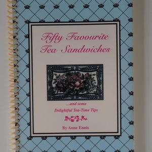 May include: A spiral-bound cookbook titled "Fifty Favourite Tea Sandwiches" with a light blue cover featuring a repeating black floral pattern. The title is in pink script, and the book includes tea-time tips.