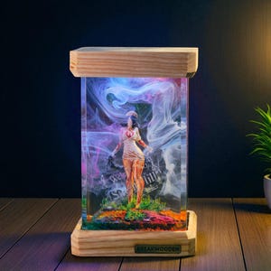 Op de afbeelding: Een houten kunstwerk van hars met een verpleegsterfiguur in een rokerige, kleurrijke display. De basis en het bovenframe zijn van lichtgekleurd hout. Het beeldje staat op een kleurrijke basis met de tekst "Welcome to Silent Hill".