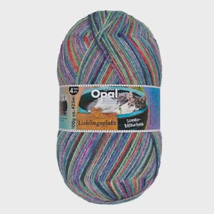 Puede incluir: Ovillo de lana Opal multicolor, con tonos azules, verdes, rojos y morados. La etiqueta muestra un gato y las palabras "Lieblingsplatz" y "Sonnen-Badewanne". El ovillo pesa 100g y contiene aproximadamente 425m de hilo.