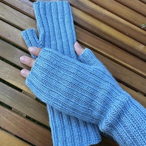 Könnte beinhalten: Ein Paar hellblaue Fingerhandschuhe aus Rippstrick. Die Handschuhe bedecken Hand und Handgelenk, mit einer Öffnung für den Daumen. Die Handschuhe werden auf einer Holzoberfläche gezeigt.