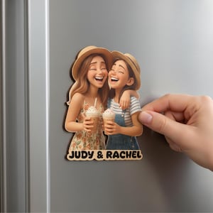 Pu&ograve; includere: Un magnete in legno con due donne sorridenti con cappelli di paglia, che tengono caff&egrave; freddi. Una indossa un vestito floreale, l'altra una camicia a righe e una salopette. Il magnete ha il testo "JUDY & RACHEL" in basso.