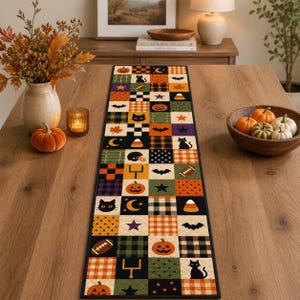 May include: A rectangular table runner featuring a patchwork design of squares with Halloween and autumn motifs including pumpkins, black cats, bats, footballs, goalposts, stars, moons, candy corn, and plaid patterns in orange, black, green, and purple.