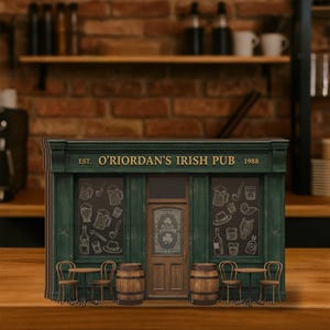Op de afbeelding: Een miniatuurmodel van een Ierse pub met een groene gevel en de tekst "O'Riordan's Irish Pub 1988". De ramen tonen krijttekeningen van pub-items. Twee kleine tafels en stoelen staan voor de pub.